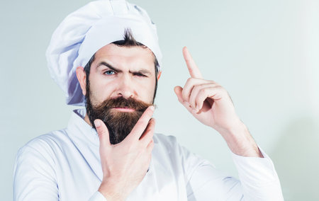 Professional chef pointing finger up. Pensive bearded man in cook uniform. Cooking food new ideasの写真素材