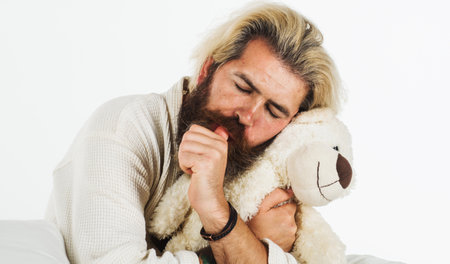 Man sleep with teddy bear at bedroom. Bearded guy hug soft toy relaxing in bed. Sweet dreamsの写真素材