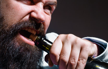 Bearded man trying to open bottle of champagne or wine. Man pull out cork with teeth. close upの写真素材