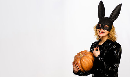 Happy girl in rabbit black mask with pumpkin. Woman in halloween bunny costume with jack-o-lanternの写真素材