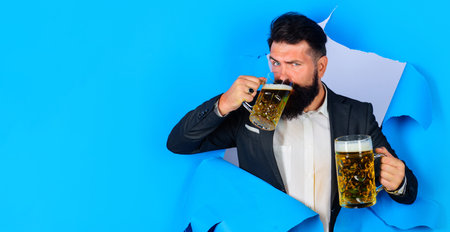 Oktoberfest. Bearded man drinking beer looking through paper hole. Stylish male with mugs of aleの写真素材