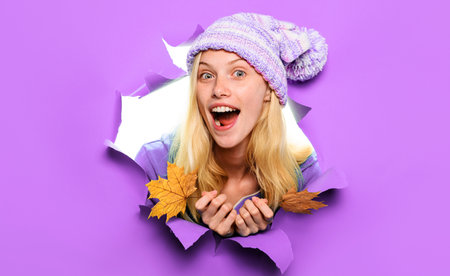 Surprised model in knitted hat with autumn leaves looking through paper. autumn saleの写真素材