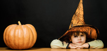 Child in witch hat with pumpkin. Preparation for Halloween celebration. Kids trick or treatの写真素材