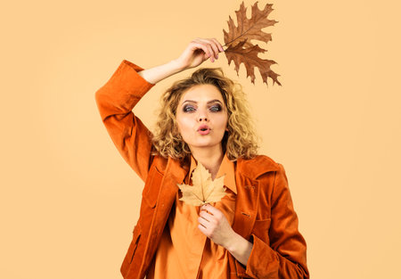 Autumn fashion girl with fall leaves. Sensual woman in orange jacket sends air kissの写真素材