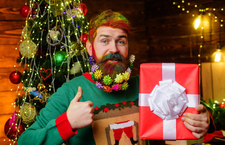 Bearded man with present gift box showing thumb up. Wish you merry Christmas. New year holidaysの写真素材