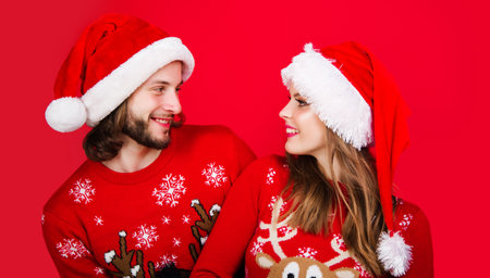 Smiling young Santa couple friends man woman in red sweater and Christmas hat. New Year celebrationの写真素材