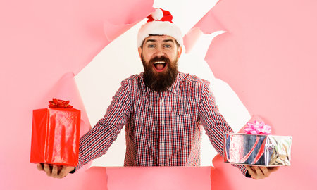 Bearded man in Santa hat and checkered shirt with gifts gifts boxes looking through paper holeの写真素材