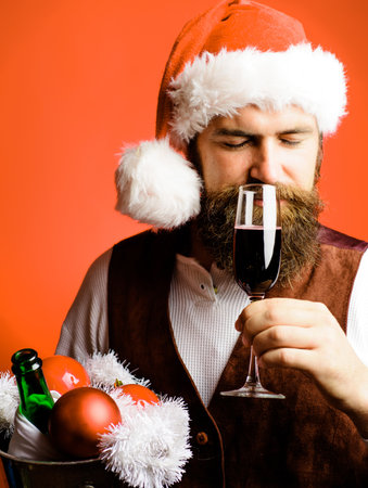 Please bearded man in Santa hat smelling red wine. Christmas or New year party. Winter holidaysの写真素材