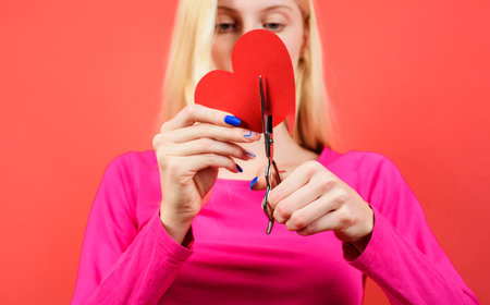 Girl cuts red heart with scissors. Breaking relations, quarrels and divorce. Betrayal of othersの写真素材