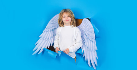 Valentine banner. Cute child in white wings looking through paper hole. Cupid boy in angel costumeの写真素材