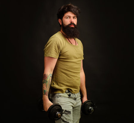 Bodybuilding. Muscular bodybuilder lifting dumbbells. Sports lifestyle. Handsome athletic man doing weightlifting with dumbbells. Bearded man doing strength exercise with dumbbells at fitness club.の写真素材