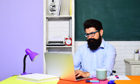 Serious school teacher or businessman working with laptop at workplace. Learning, education. Bearded student in glasses preparing for exam or test at university. Male student taking notes on computer.の写真素材