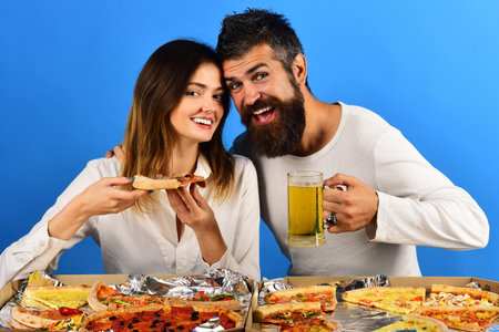 Pizza time. Couple in love eating pizza and drinking beer. Man drinking cold beer, woman eating delicious pizza. Romantic young couple male and female in casual clothes eating pizza and drinking beerの写真素材