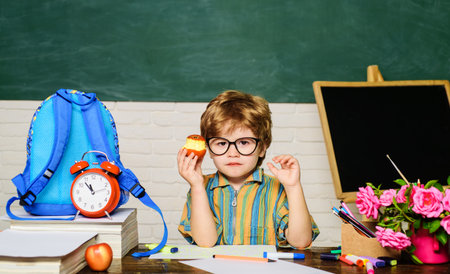 Lunch time. Cute serious schoolboy sitting at table and eating apple in classroom. School break....