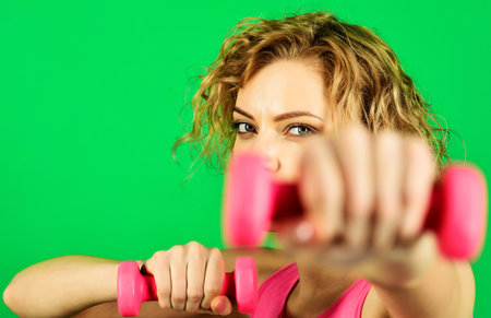 Health, sport and fitness. Sporty girl pumping her arm muscles during strength training. Woman doing exercises with dumbbells, selective focus. Athletic girl makes fitness exercising withの写真素材