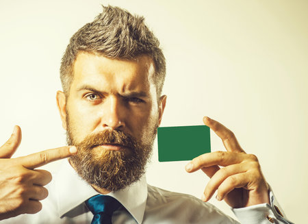 Serious businessman pointing finger at credit or debit card. Handsome bearded man shows mockup template bank card. E-commerce, payment transaction, e-money. Copy space for advertising banking serviceの写真素材