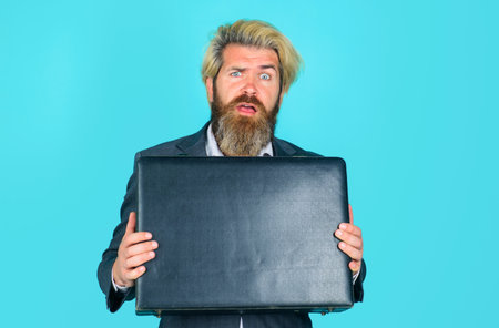 Confused bearded man with leather briefcase. Office worker, businessman in classic formal suit with briefcase. Handsome male with stylish hairdo holds business briefcase. Business man with briefcase.の写真素材
