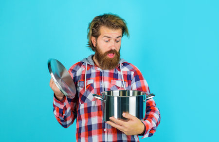 Handsome man with pot. Bearded man in plaid shirt with saucepan or pan. Kitchenware. Cooking utensils. Surprised man in checkered shirt opens lid of cooking pot. Man preparing healthy food in kitchen.の写真素材