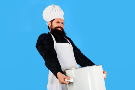 Male chef carrying heavy big pot at restaurant kitchen. Cooking and culinary. Bearded cook prepares food in saucepan. Healthy food menu. Professional chef in uniform with pan or casserole. Cookware.の写真素材