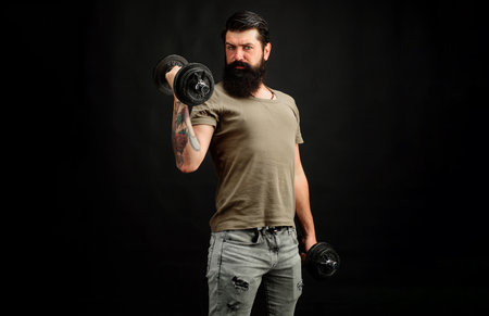 Sporty man lifting dumbbells. Sport man or trainer exercising with dumbbells in gym. Fit guy working out in gym. Sportsman lifting dumbbells. Athletic young male fitness model training with dumbbells.の写真素材