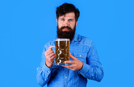 Oktoberfest festival. Bearded man in denim shirt with large craft beer mug. Germany tradition. Stylish man with glass of cold beer. Handsome man drinking draft beer in pub or bar. Alcohol and leisure.の写真素材