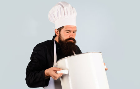 Male chef or cook in uniform holding large saucepan or pot and smelling meal. Enjoying delicious food smell. Chef man in apron holds casserole or big cooking pan and sniff aroma dish with eyes closed.の写真素材