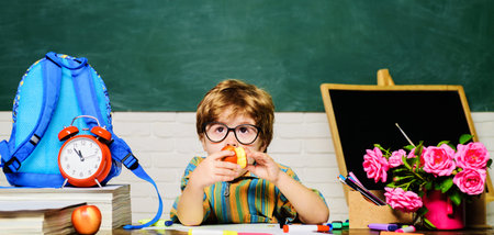 School lunch. Cute schoolboy in glasses sitting at desk and eating apple. Delicious food for kids...
