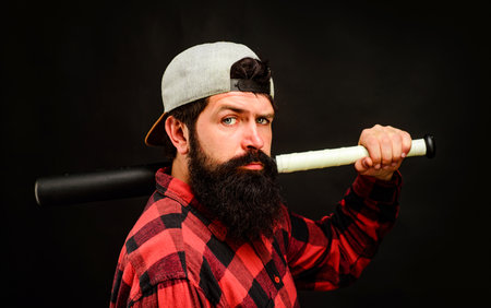 Bearded man in plaid shirt with baseball bat on shoulder. Handsome male in checkered shirt with...