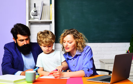 Private lesson. Primary school pupil having lesson with private tutors. Education, learning. Male and female teacher with schoolboy at desk in classroom. Couple teachers helping child doing homework.の写真素材