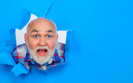 Shocked bearded man looking through paper hole. Surprised mature man making hole in paper. Copy space for advertising, to insert text or slogan. Discount, sale, season salesの写真素材