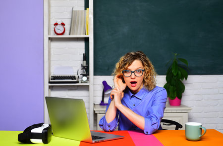 Young surprised businesswoman or female office worker with laptop computer at workplace. Student girl preparing for exam or test at university. Studying with online courses or webinar. Emotional faceの写真素材