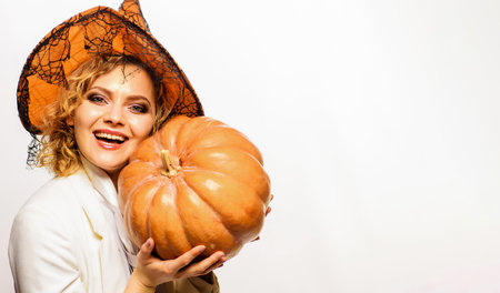 Happy girl in witch hat with pumpkin. Halloween holidays. Smiling woman with jack-o-lanternの写真素材