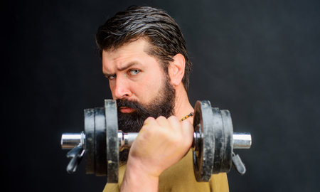 Portrait of bearded man exercising in gym lifting dumbbell. Healthy lifestyle and strength exercise at fitness club. Bodybuilder pumping biceps with dumbbell. Strong man using dumbbell during workoutの写真素材