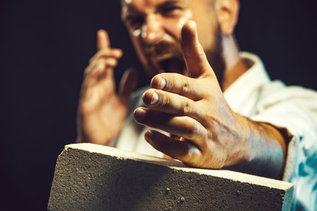 Karate master instructor breaks brick, selective focus on hand. Man hand breaking concrete brick. Screaming karate fighter smashes concrete slab. Strong angry karate man in kimono shows kick by handの写真素材