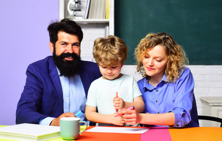 Back to school. Primary school pupil having lesson with private tutors. Couple teachers helping child doing homework. Education, learning. Male and female teacher with schoolboy at desk in classroom.の写真素材