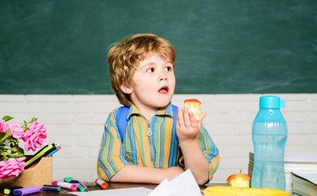 School lunch. Little schoolboy eating apple during break at school. Tasty food for kids health. Cute child sitting at table and eating healthy food. Elementary school student at lunch time in class.の写真素材