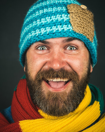 Closeup portrait of happy man in warm hat and scarf. Bearded man in winter clothing. Autumn-winter fashion for men. Winter man. Style, fashion. Handsome stylish male in colorful scarf and knitted hatの写真素材