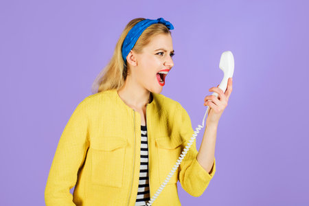 Shouting woman into old phone handset. Emotions and feelings. Angry pin-up girl in yellow jacket and...