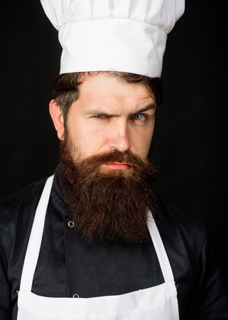 Closeup portrait of serious male chef in uniform. Cooking man. Culinary, cooking and food preparation. Professional chef, cook or baker in kitchen. Handsome bearded man in uniform, chef hat and apronの写真素材