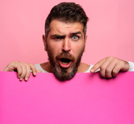 Surprised man pointing down at advertising board with empty space for text, mockup. Handsome male with blank signboard, advertising banner. Bearded man with advertising posterの写真素材