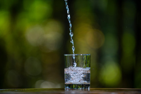 Glass and water with pouring on the nature background. Water pouring into glass on wooden table...