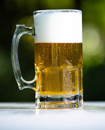 Beer in glass on green bokeh background. Beer pouring with foam close up. Beer glass summer...