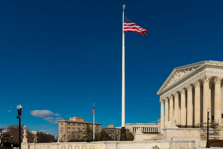 American flag flying above supreme court architecture. Judicial branch concept with historic neoclassical building. Democracy and legal system symbol in capital city.の写真素材