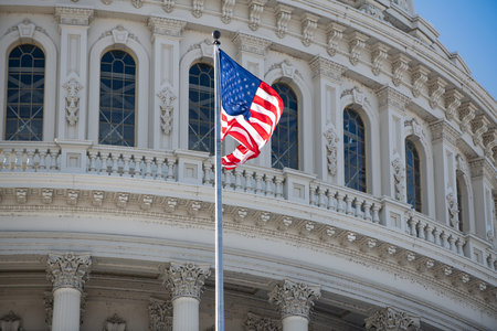 Capitol with american flag under blue sky. American flag near capitol with historic architecture. Us flag on capitol as national symbol. Capitol with american flag for democracy background.の写真素材