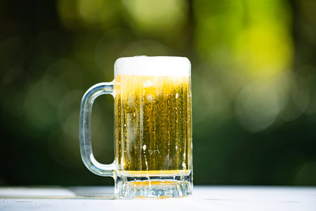Beer in glass on green bokeh background. Beer with foam close up. Lager beer in glass, summer...