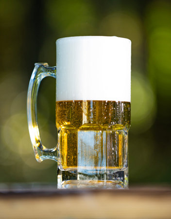 Beer rests in mug. Beer carries thick foam. Beer sparkles inside glass. Beer looks inviting.
