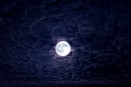 Bright full moon with dramatic night clouds. Moonlight on dark cloudy sky. Full moon in deep blue...