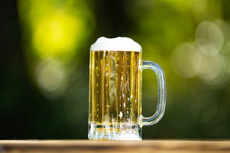 Beer in glass on green bokeh background. Beer with foam close up. Beer glass summer relaxation. Craft beer taste. Beers cup.の写真素材