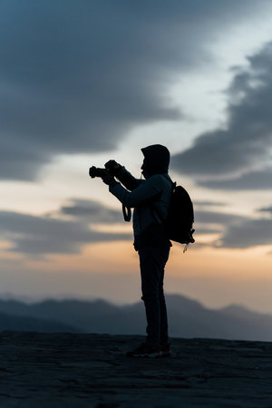 Silhouette of photographer with camera in hand on the top of mountain