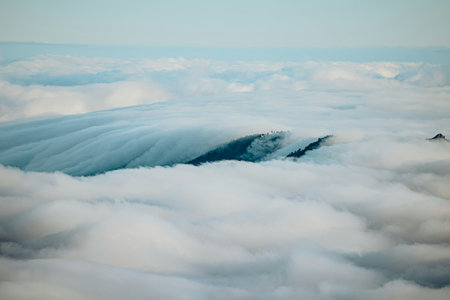 Aerial view of clouds and mountain peaks in the blue sky.